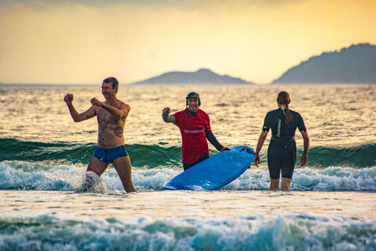 aluno homem e instrutor ernesto os dois com os braços levantados em sinal de comemoração na beira do mar na praia da barra da lagoa em florianianópolis