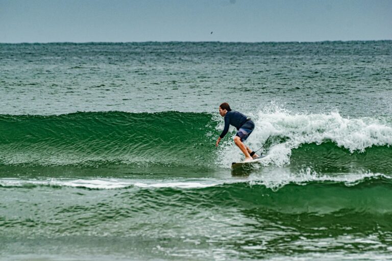 aluno homem jovem de pé em uma prancha surfando na praia da barra da lagoa em florianianópolis