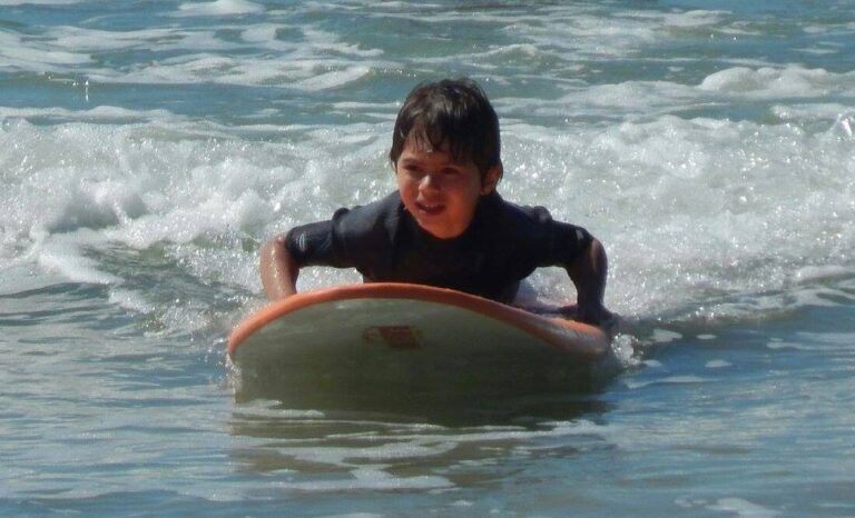 aluno criança da nexus surf school deitado na prancha um pouco antes de se levantar na praia da barra da lagoa em florianianópolis